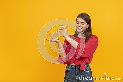 Young woman to red blouse holds grocery cart on her hand. Portrait of girl with shopping cart on the palm of her hand on yellow Stock Photo