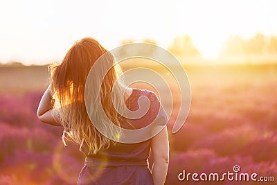 Young woman touching her long sombre hair looking at lavender field at sunset Stock Photo