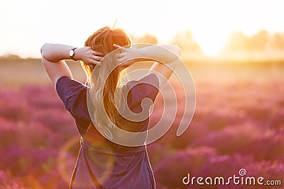 Young woman touching her long sombre hair looking at lavender field at sunset Stock Photo