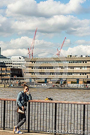Young Woman Tourist Looking Bored Or Lost Leaning on a Fence Overlooking the River Thames Deep Editorial Stock Photo