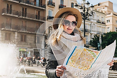 Young woman tourist stands on street of ancient European city and holds map. In background is beautiful building. Stock Photo