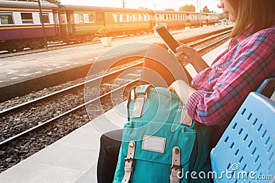 Young woman traveler and backpack waiting railway at train station, Young woman sitting with using smartphone at the train station Stock Photo