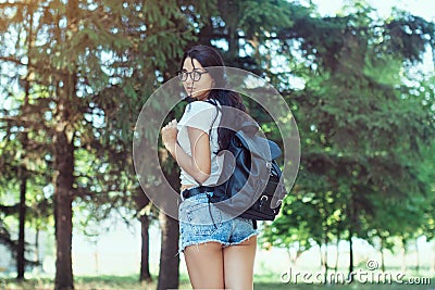 Young woman traveler with backpack standing alone in forest. Hipster girl in sunny woods Stock Photo