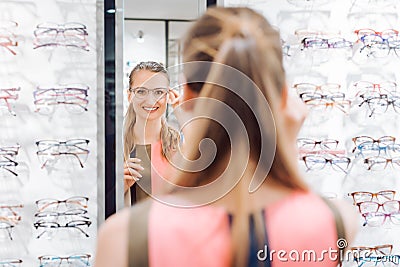 Young woman trying fashionable glasses in optometrist store Stock Photo