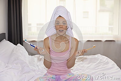 A young woman is trying to choose by comparing modern electric and eco-friendly bamboo toothbrushes Stock Photo