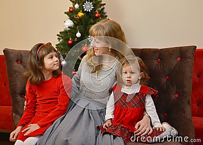The young woman and two girls sit against the background of a New Year tree Stock Photo