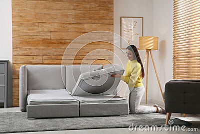Young woman unfolding sofa into a bed in room. Modern interior Stock Photo
