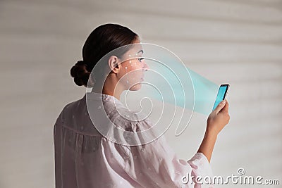 Young woman unlocking smartphone with facial scanner near white wall. Biometric verification Stock Photo