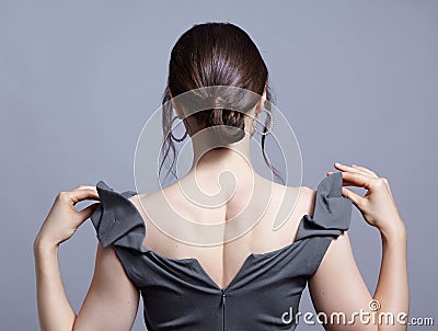 Young woman with unzipped zipper on the dress. Bunette female rear view with hair knot and earrings in the ears Stock Photo