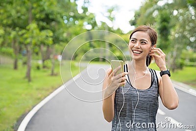 Young woman using phone for listening to music. Fitness runner girl listening to music with earphones on phone wearing smartwatch. Stock Photo