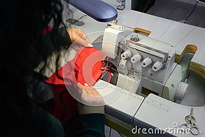 Young woman using professional overlock sewing machine in workshop studio. Equipment for edging, hemming or seaming Stock Photo