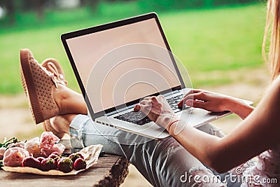 Young woman using and typing laptop computer at rough wooden table with coffee cup, strawberries, bouquet of peonies flowers, Stock Photo