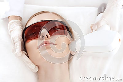 Young woman in uv protective glasses receiving laser skin care on face Stock Photo