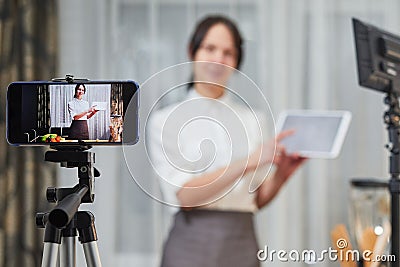 Vlogger recording video for food channel. Female vlogging with her mobile phone mounted on a tripod and a light stand Stock Photo