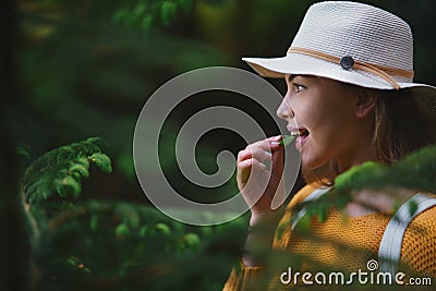 Young woman on a walk outdoors in forest in summer nature, eating spruce shoots. Stock Photo