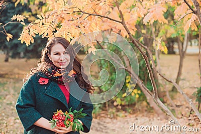 A young woman walks in the autumn Park. Brunette woman wearing a green coat. She is holding a bouquet of yellow leaves Stock Photo