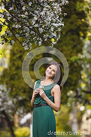 Young woman weared in long green dress in a blooming apple garden Stock Photo