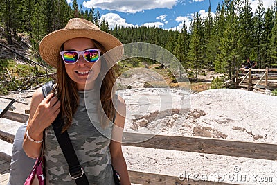 Young woman wearing a camoflauge outfit and sun hat poses at the mud pots at Artist Paint Pots in Yellowstone Stock Photo
