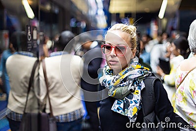 Young woman wearing colorful scarf waiting on the platform of a urban metro station for train to arrive. Public Stock Photo