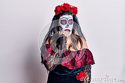 Young woman wearing day of the dead costume over white looking stressed and nervous with hands on mouth biting nails Stock Photo
