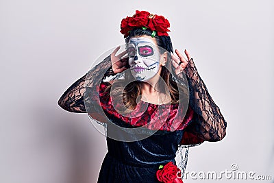 Young woman wearing day of the dead costume over white trying to hear both hands on ear gesture, curious for gossip Stock Photo