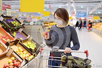 Young woman wearing disposable medical mask shopping in supermarket during coronavirus pneumonia outbreak Stock Photo