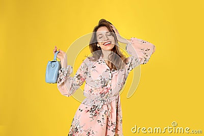 Young woman wearing floral print dress with handbag on yellow background Stock Photo