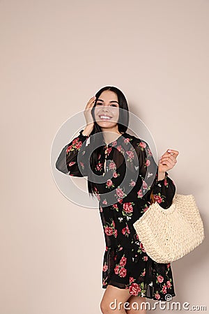 Young woman wearing floral print dress with straw bag on background Stock Photo