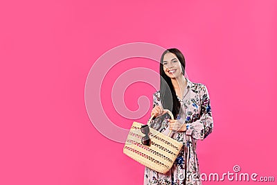 Young woman wearing floral print dress with straw bag on background. Space for text Stock Photo