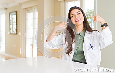 Young woman wearing medical coat at the clinic as therapist or doctor smiling confident showing and pointing with fingers teeth Stock Photo