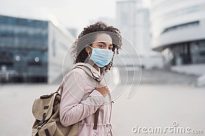 Young woman wearing protective face mask in a city. Masked african-american teenage student girl on a city street. Stock Photo