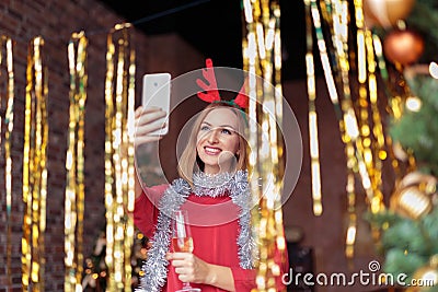 Young woman wearing red dress with antler deer headband taking selfie on Christmas party Stock Photo