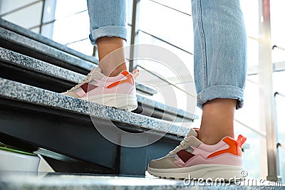 Young woman wearing stylish sneakers on stairs indoors, closeup Stock Photo