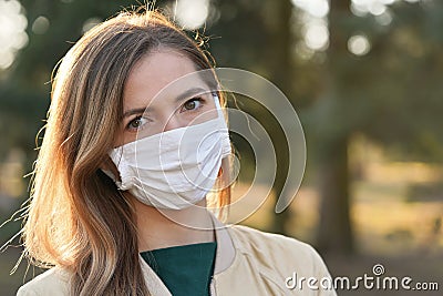 Young woman wearing white cotton virus mouth nose mask, blurred park and trees background, closeup face portrait, coronavirus Stock Photo