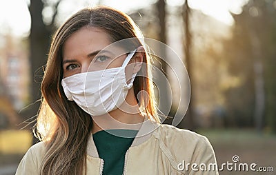 Young woman wearing white cotton virus mouth nose mask, blurred park and trees background, closeup face portrait, coronavirus Stock Photo