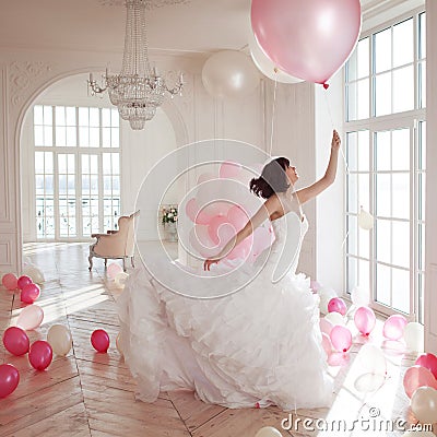 Young woman in wedding dress in luxury interior flies on pink and white balloons. Stock Photo