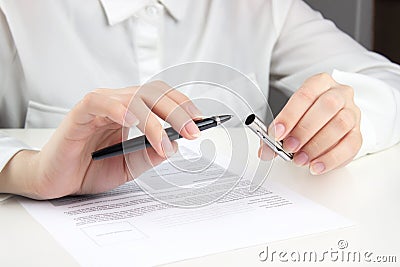 A young woman in a white blouse removes the cap from a pen to start filling out documents Stock Photo