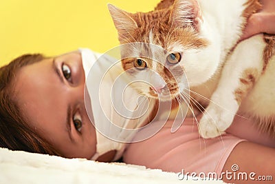 Young woman in white cloth virus face mask playing with her cat, detail on feline eyes, owner blurred in background Stock Photo