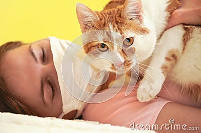 Young woman in white cloth virus face mask playing with her cat, detail on feline eyes, owner blurred in background Stock Photo