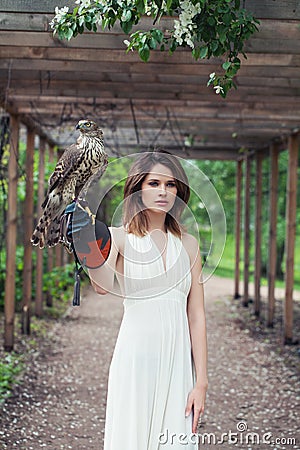 Young woman in white dress holding hawk bird outdoor Stock Photo