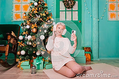 Young woman in white, fluffy headphones in Christmas decorations with a phone in her hands. a smartphone Stock Photo