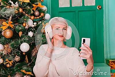 Young woman in white, fluffy headphones in Christmas decorations with a phone in her hands. a smartphone Stock Photo