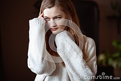Young woman in a white oversized sweater holding her hands near her face and thinking Stock Photo