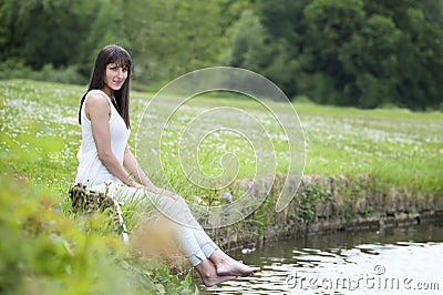 Young woman in white seated at the lake Stock Photo