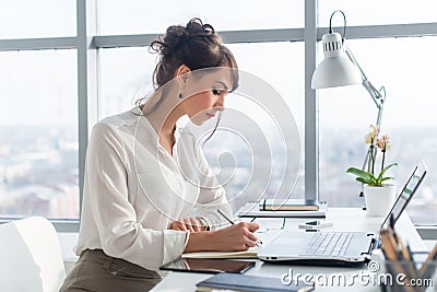 Young woman working as an office manager, planning work tasks, writing down her schedule to planner at the workplace. Stock Photo