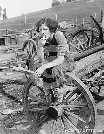 Young woman in working jeans sitting on wheel eating an apple Stock Photo