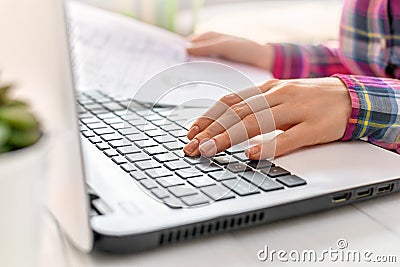 Young woman works on laptop at home. Hands holding a sheet of document and typing on a keyboard closeup. Remote work concept, Stock Photo