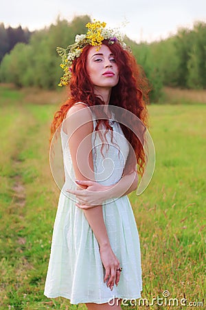 Young woman in wreath and short dress poses on meadow at Stock Photo