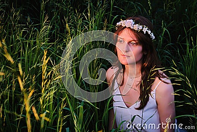 A young woman with a wreath of white flowers in the tall grass and reeds. A girl in a white dress who looks like a mermaid from a Stock Photo