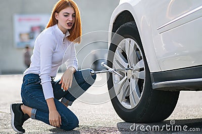 Young woman with wrench changing wheel on a broken car Stock Photo